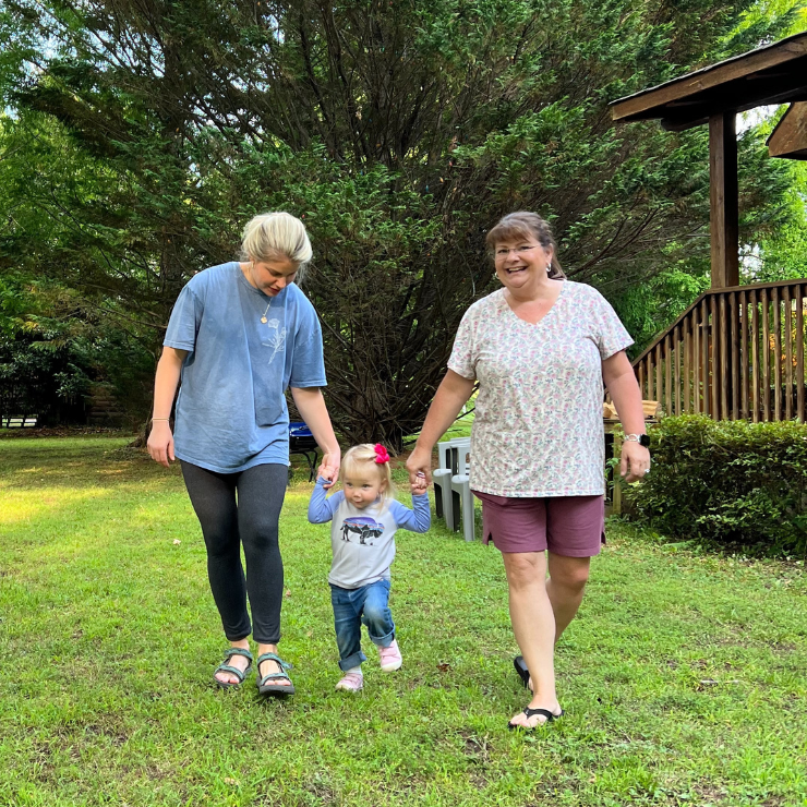 A little girl walking holding the hands of her mom and grandmother. 