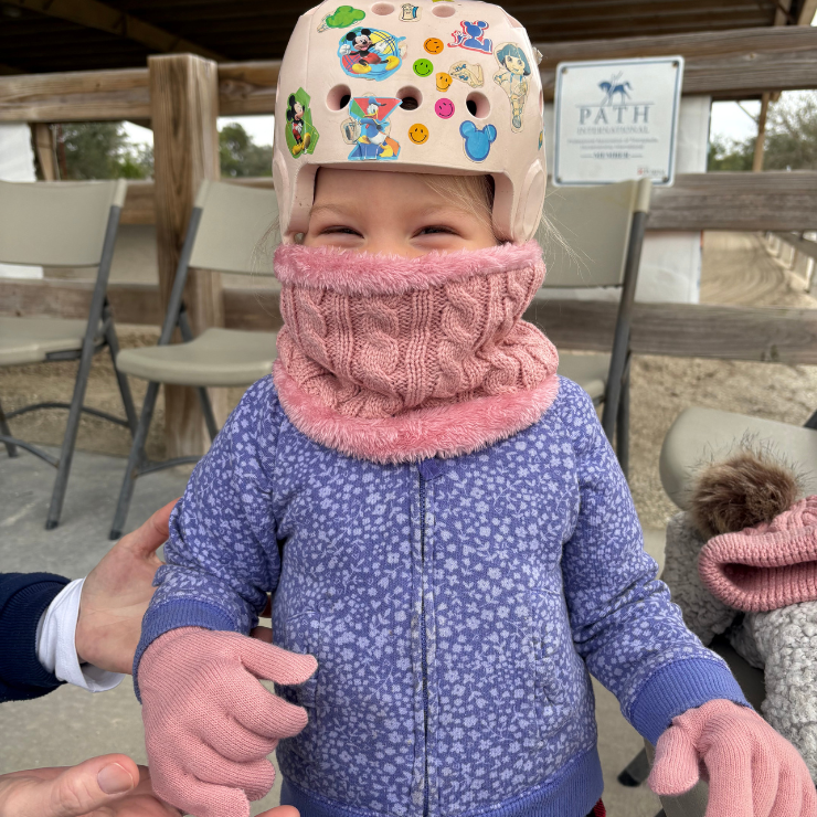 A little girl with a stickered helmet on bundled up in the cold.