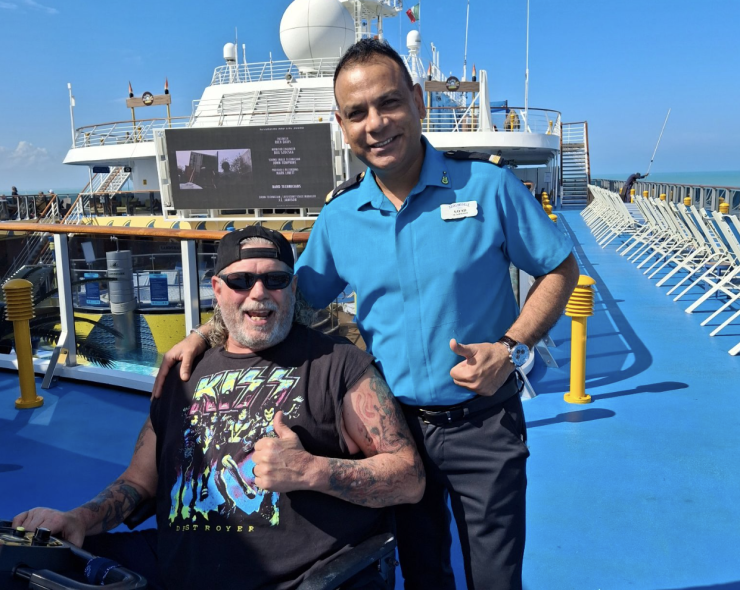 A man in a wheelchair on a cruise ship deck with a worker from the boat giving thumbs up