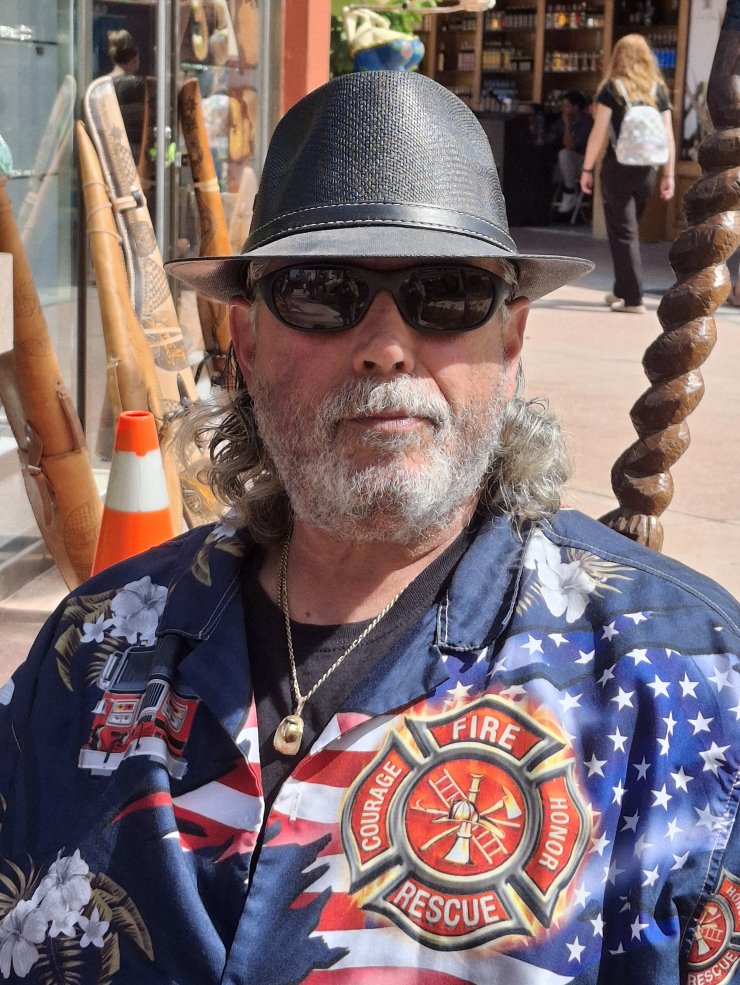 Person wearing a fedora and sunglasses with a shirt featuring an American flag and firefighter emblem.