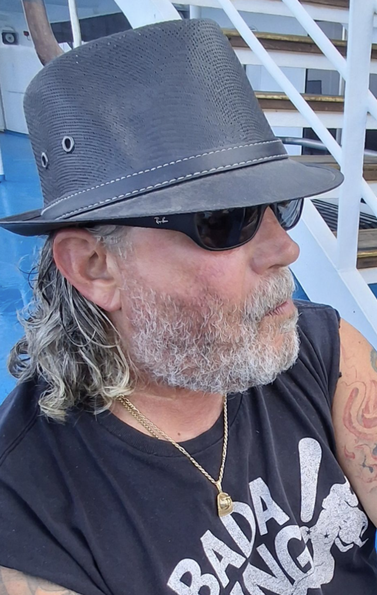 A man with grey hair and beard in sunglasses with a black fedora 