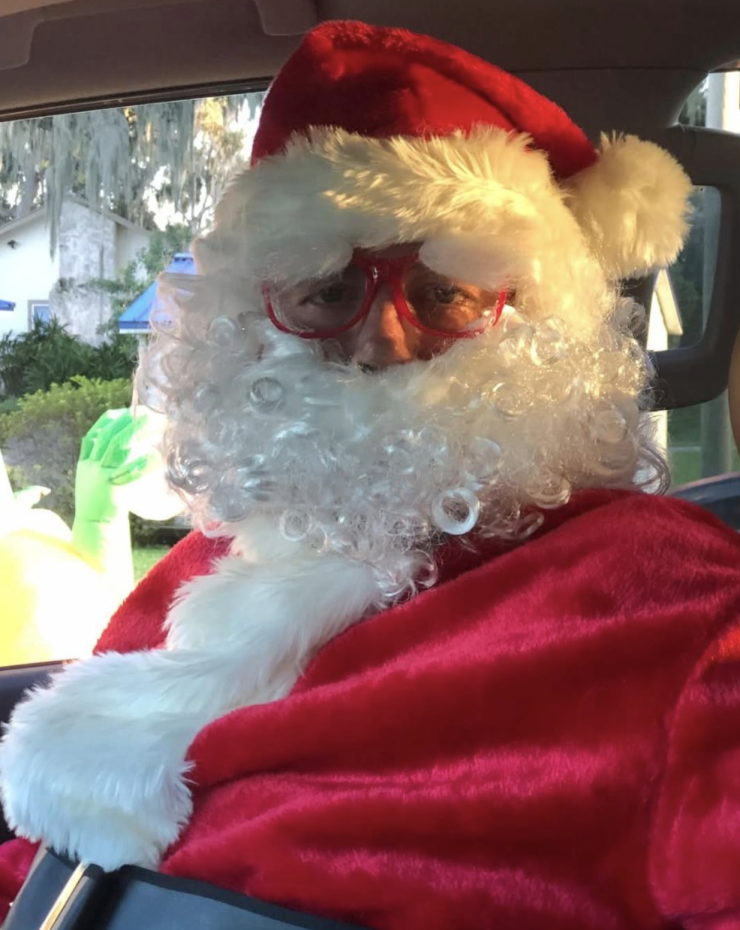 Person dressed as Santa Claus with red-rimmed glasses inside a vehicle.