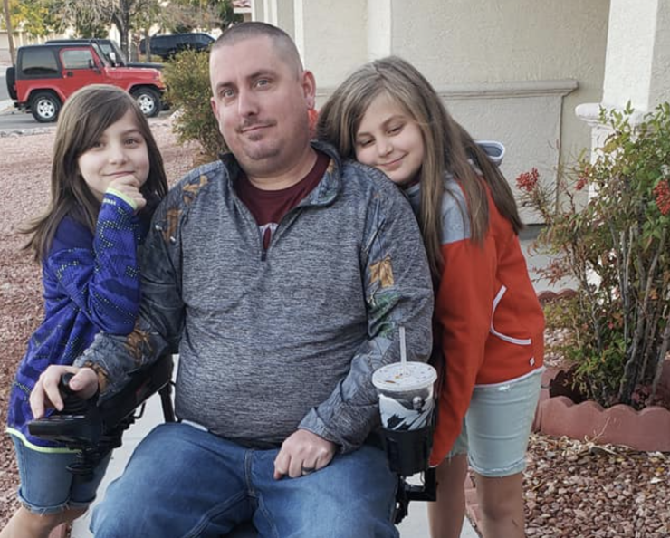 A man in a motorized wheelchair with two young girls standing beside him.