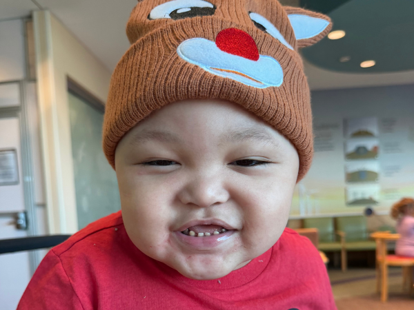 Smiling child in a brown reindeer hat and red shirt, photographed indoors.